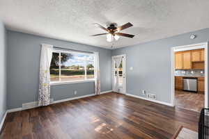 Unfurnished living room with ceiling fan, dark wood finished floors, and a textured ceiling