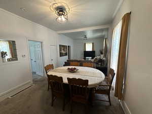 Dining room with dark colored carpet, ornamental molding, and a textured ceiling