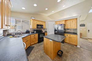 Kitchen featuring black appliances, vaulted ceiling, tasteful backsplash, dark countertops, and a center island