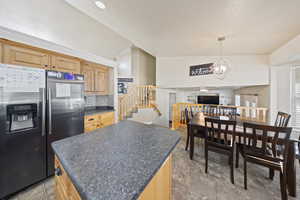 Kitchen with stainless steel fridge, dark countertops, light brown cabinets, a chandelier, and tasteful backsplash