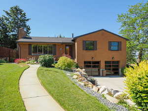 View of front of home with an attached garage, concrete driveway, brick siding, and a chimney