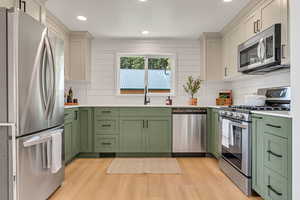 Kitchen featuring green cabinetry, appliances with stainless steel finishes, light wood-style floors, light countertops, and recessed lighting
