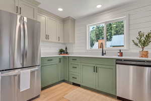 Kitchen featuring stainless steel appliances, green cabinetry, light countertops, light wood finished floors, and recessed lighting