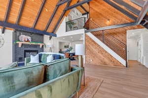 Living room with high vaulted ceiling, wood finished floors, beamed ceiling, wood walls, and a brick fireplace