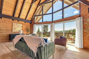 Bedroom featuring wooden walls, high vaulted ceiling, multiple windows, access to exterior, and wood finished floors