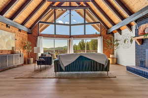Bedroom with wooden walls, a wood ceiling with exposed beams, high vaulted ceiling, a brick fireplace, and wood finished floors