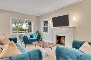 Living area with ornamental molding, a fireplace with flush hearth, and light wood-style flooring