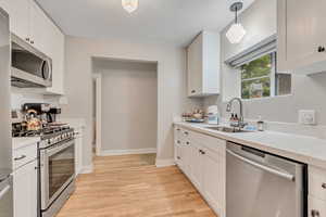 Kitchen with appliances with stainless steel finishes, light wood-style floors, light countertops, white cabinetry, and hanging light fixtures