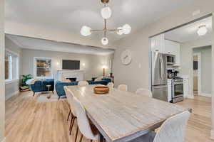 Dining room featuring light wood-style flooring, a chandelier, a fireplace, and crown molding