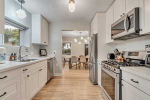Kitchen with stainless steel appliances, light wood-style flooring, white cabinetry, light countertops, and hanging light fixtures