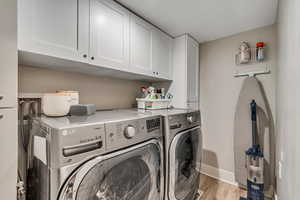 Laundry room featuring washer and clothes dryer, cabinet space, and light wood-type flooring