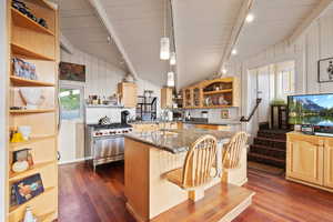 Kitchen featuring rail lighting, open shelves, dark wood-type flooring, vaulted ceiling, and an island with sink