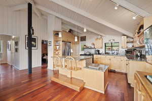 Kitchen with open shelves, rail lighting, appliances with stainless steel finishes, a kitchen island with sink, and light brown cabinets
