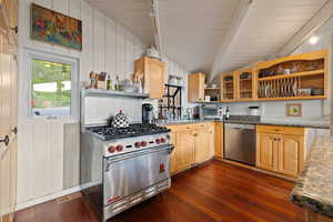 Kitchen featuring appliances with stainless steel finishes, open shelves, dark wood-type flooring, glass insert cabinets, and light brown cabinetry