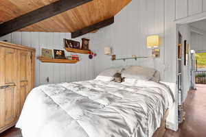 Bedroom with wood finished floors, a wooden ceiling with exposed beams, and wooden walls