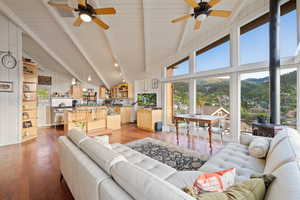 Living area featuring ceiling fan, wood-type flooring, a wood stove, a wooden ceiling with exposed beams, and high vaulted ceiling