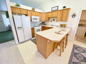 Kitchen featuring white appliances, a peninsula, light countertops, high vaulted ceiling, and a kitchen bar