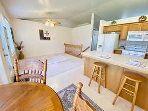 Kitchen with white appliances, lofted ceiling, a breakfast bar, light carpet, and a ceiling fan
