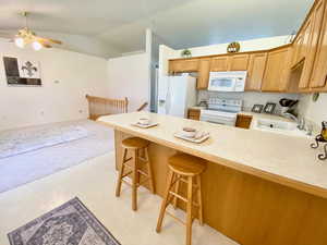 Kitchen featuring white appliances, a peninsula, lofted ceiling, ceiling fan, and light countertops