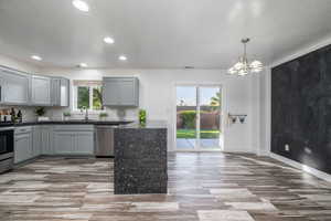 Kitchen with stainless steel appliances, gray cabinetry, wood finished floors, recessed lighting, and a chandelier