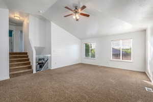 Unfurnished living room with carpet, a ceiling fan, vaulted ceiling, and stairway