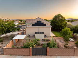 Property exterior at dusk with a gate, roof mounted solar panels, and stucco siding