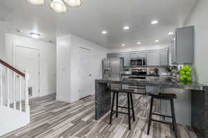 Kitchen with appliances with stainless steel finishes, gray cabinetry, a peninsula, light wood-style floors, and recessed lighting