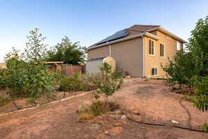 View of side of home featuring a storage unit, solar panels, and stucco siding