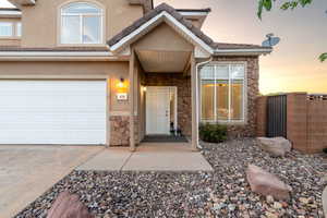 Property entrance with stone siding, driveway, stucco siding, and an attached garage