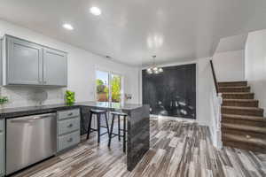 Kitchen with dishwasher, gray cabinetry, a peninsula, wood finished floors, and recessed lighting