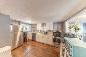 Kitchen featuring stainless steel appliances, dark wood-style flooring, a textured ceiling, white cabinets, and light stone countertops