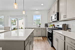 Kitchen with stainless steel appliances, gray cabinetry, light wood-type laminate flooring, decorative backsplash, and recessed lighting