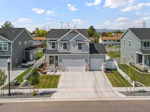 View of front of property with board and batten siding, a residential view, concrete driveway, stone siding, and roof with shingles