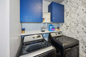 Laundry room featuring washing machine and dryer, cabinet space, and wallpapered walls
