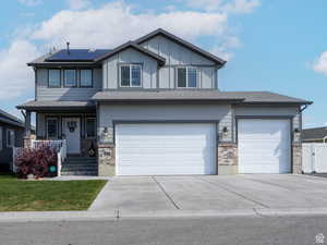 View of front of property with driveway, covered porch, roof mounted solar panels, an attached garage, and brick siding