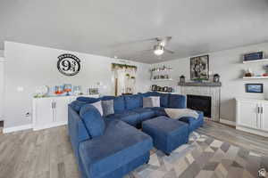 Living room featuring light wood-type flooring, ceiling fan, a textured ceiling, and a fireplace
