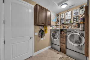 Laundry room featuring independent washer and dryer, light tile patterned floors, cabinet space, and a textured ceiling