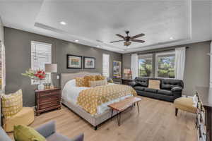 Bedroom featuring a raised ceiling, light wood-style flooring, recessed lighting, a ceiling fan, and a textured ceiling