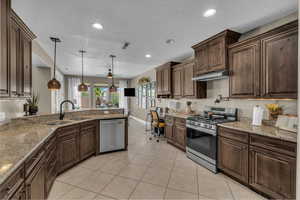 Kitchen with stainless steel appliances, under cabinet range hood, a ceiling fan, light tile patterned floors, and hanging light fixtures