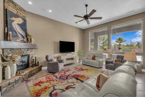 Tiled living area featuring ceiling fan, a stone fireplace, and recessed lighting