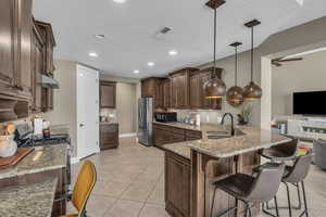 Kitchen featuring appliances with stainless steel finishes, light stone counters, light tile patterned floors, a peninsula, and a breakfast bar area