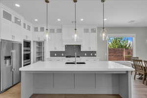 Kitchen featuring appliances with stainless steel finishes, glass insert cabinets, backsplash, light wood-style floors, and white cabinets