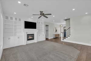 Unfurnished living room featuring built in shelves, a glass covered fireplace, recessed lighting, stairway, and light wood-type flooring