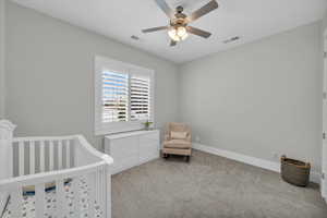 Bedroom featuring carpet floors, ceiling fan, and a nursery area