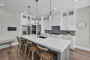 Kitchen with stainless steel appliances, wood finished floors, tasteful backsplash, a kitchen island with sink, and a kitchen bar