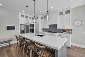 Kitchen featuring appliances with stainless steel finishes, dark wood-style floors, decorative backsplash, an island with sink, and white cabinetry