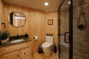 Bathroom with vanity, wood finished floors, a stall shower, wooden walls, and recessed lighting