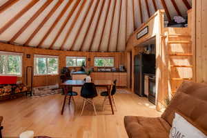 Dining room with beam ceiling, plenty of natural light, light wood-type flooring, wood walls, and high vaulted ceiling