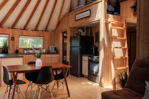 Kitchen featuring stainless steel electric stove, dark countertops, wooden walls, light wood-style floors, and freestanding refrigerator