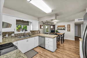 Kitchen featuring dishwasher, a peninsula, decorative backsplash, white cabinets, and light wood-style floors